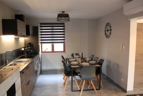 Une cuisine moderne avec un coin repas, comprenant un four encastré, une machine à café et une table à manger pour quatre personnes.