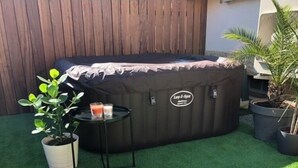 A hot tub with a cover, a small table with candles, and potted plants in a backyard.