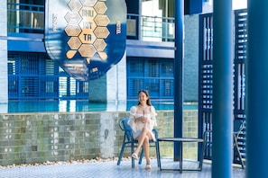 A person seated on a chair by a poolside, with a large sign overhead displaying hotel branding.