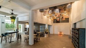 A spacious interior with a herringbone wooden floor, a central seating area with tables and chairs, hanging wicker lamps, and a ceiling fan. - Bhukitta Boutique Hotel - SHA Plus (PHUKET)