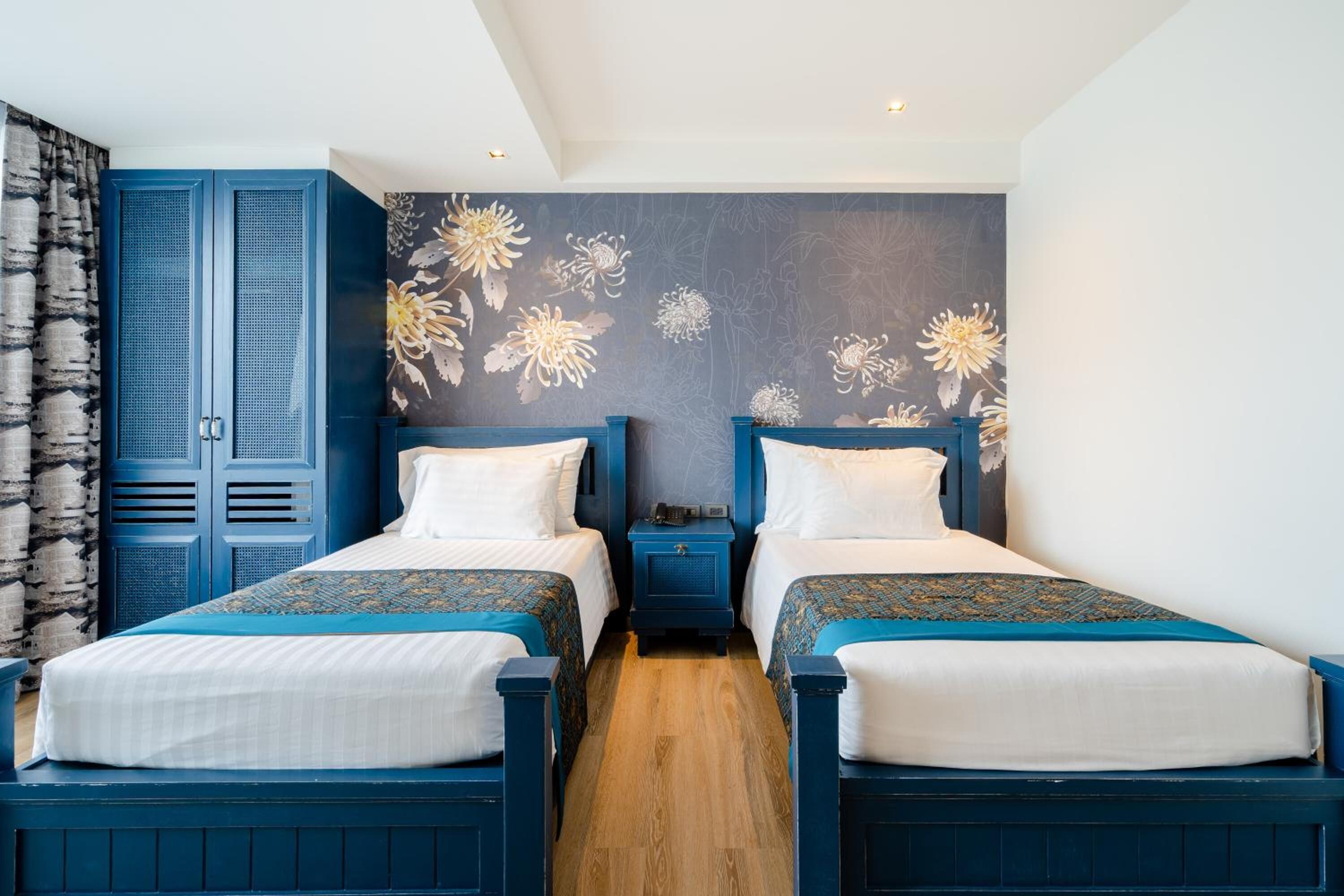 A bedroom with two beds, a wardrobe, and a floral wall mural.