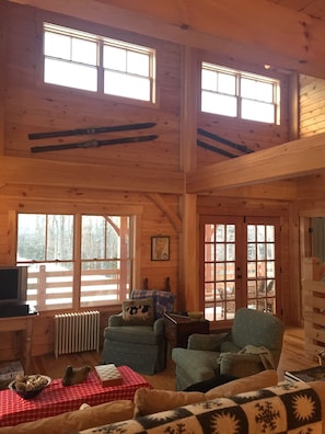 A cozy cabin interior with wooden walls, a fireplace, a television, and a dining area with a checkered tablecloth.