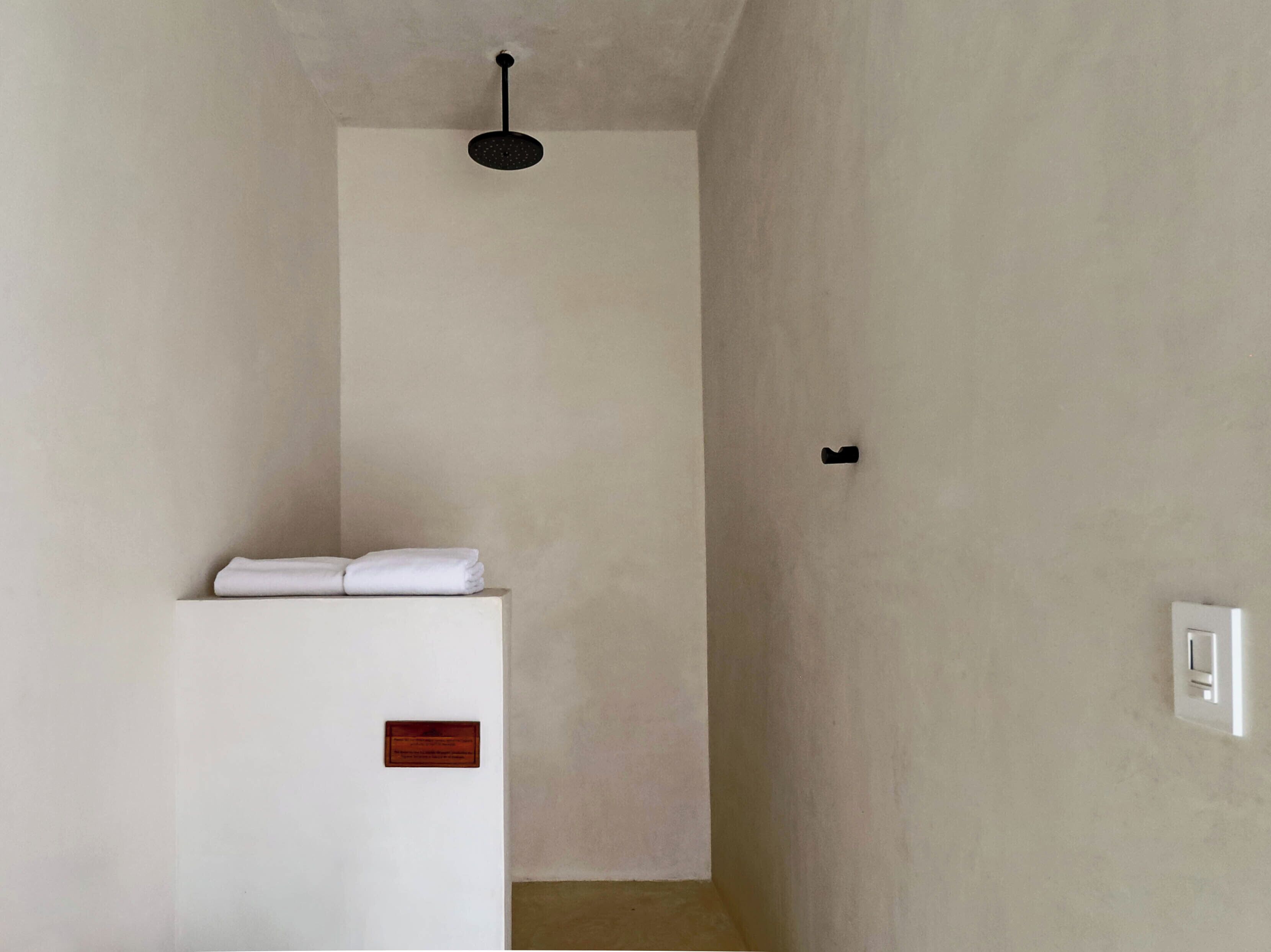 A minimalist bathroom with a white sink, a towel, a light switch, and a ceiling-mounted light fixture.
