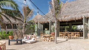 A beachside resort with thatched-roof structures, outdoor seating, and lush tropical plants. - Hotel Panamera (Tulum)