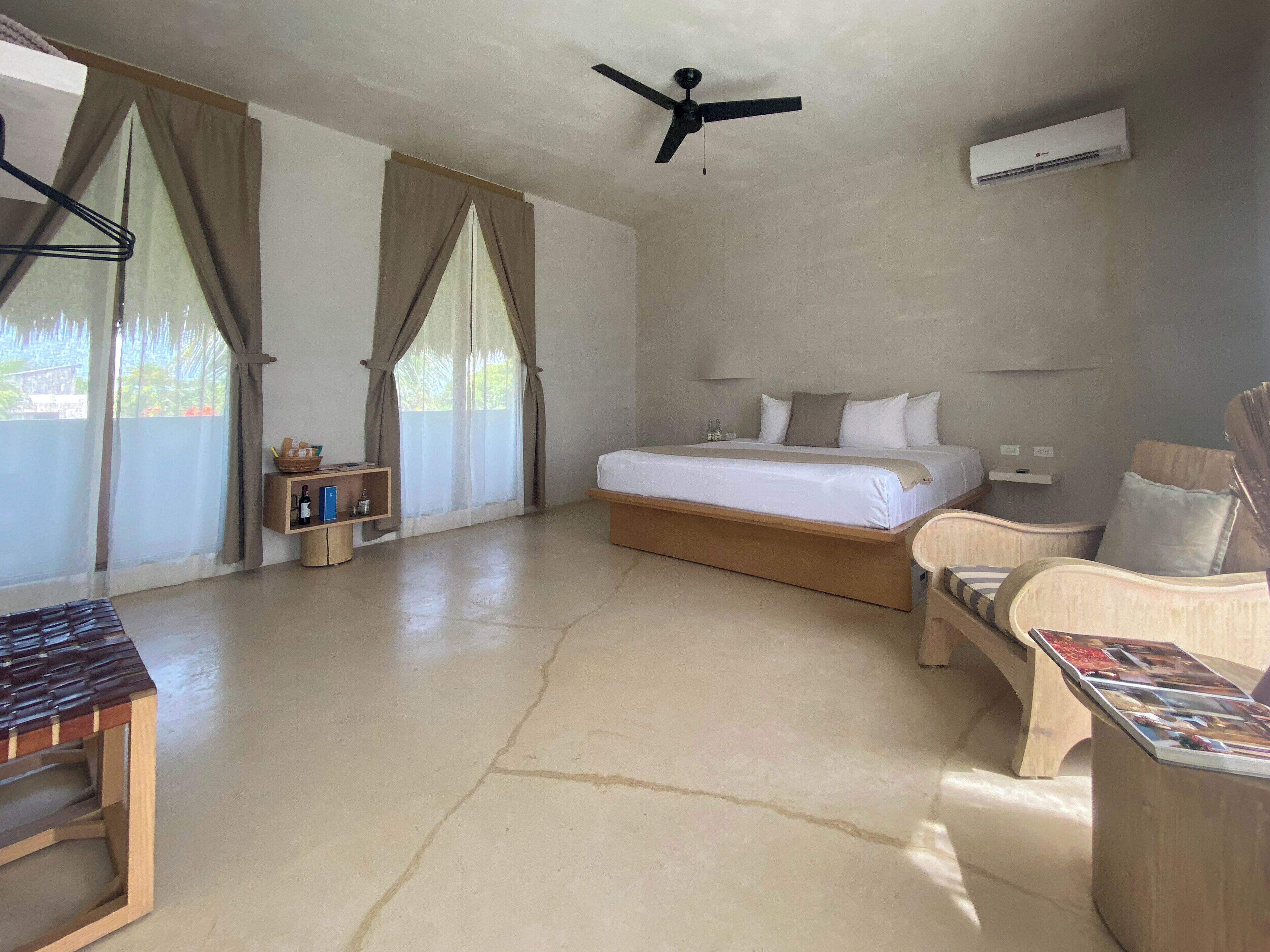 Una habitación de hotel con una cama, una silla, una mesa, un ventilador de techo y un equipo de aire acondicionado.