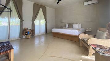 Una habitación de hotel con una cama, una silla, una mesa, un ventilador de techo y un equipo de aire acondicionado.