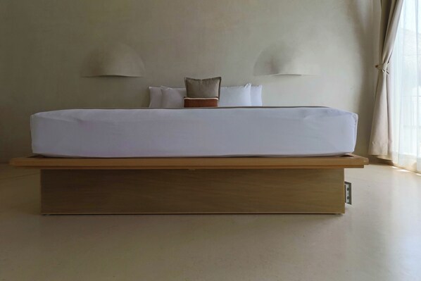 A bed with a wooden frame and white bedding, two wall-mounted lamps, and a window with curtains.