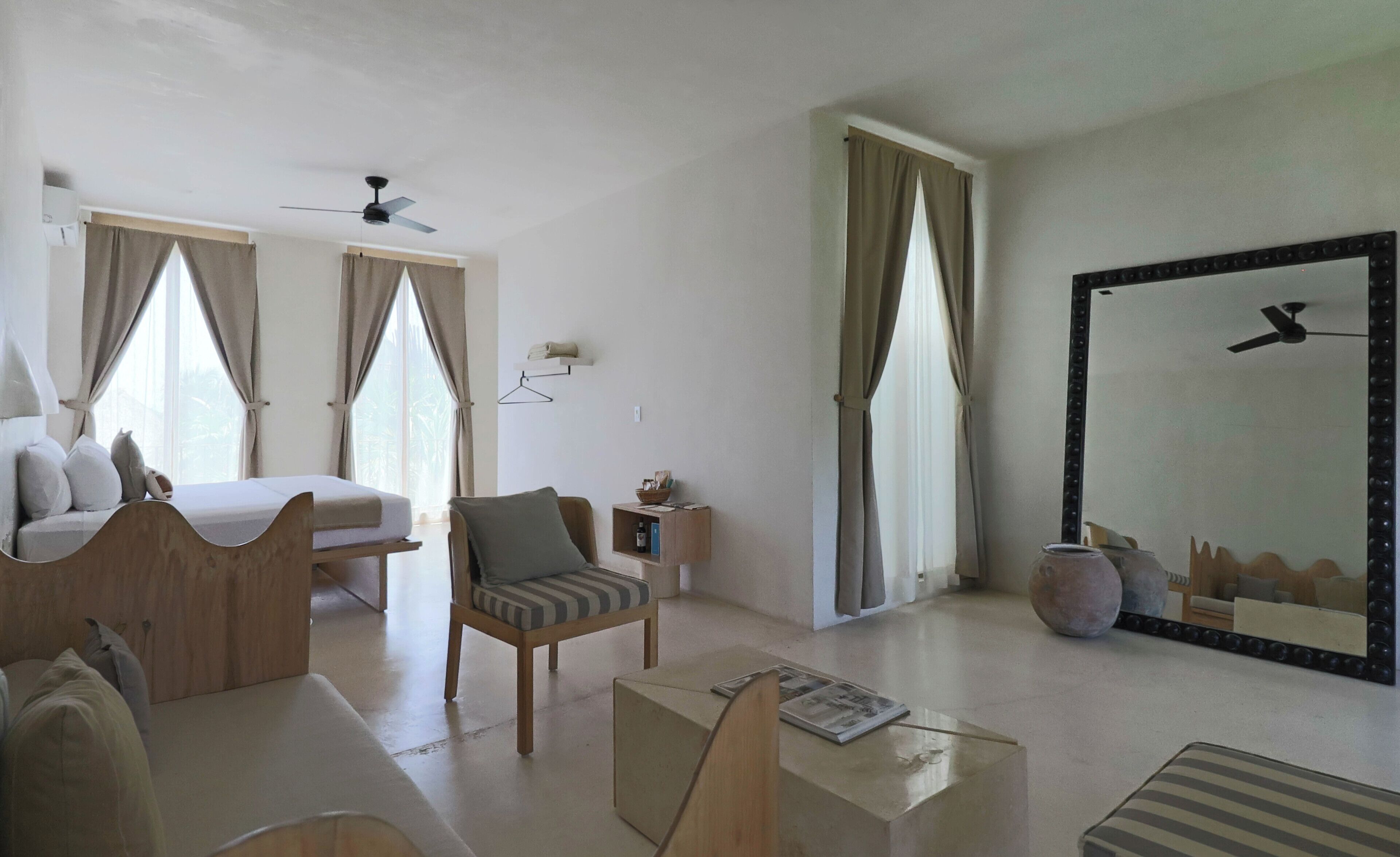 A hotel room with a bed, a chair, a small table, a mirror, and a ceiling fan.
