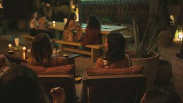 Una habitación tenuemente iluminada con un grupo de personas sentadas en sofás viendo una película en una pantalla grande.