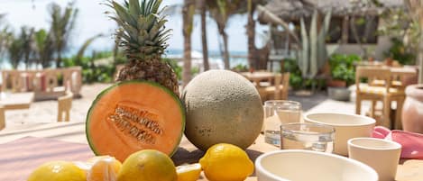 A table with a pineapple, cantaloupe, lemons, and bowls on a wooden surface.