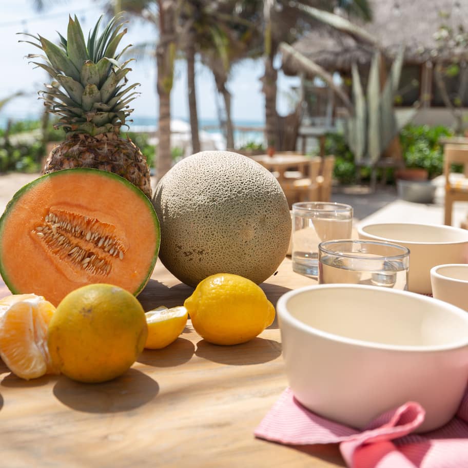 A table with a pineapple, cantaloupe, lemons, and bowls on a wooden surface.