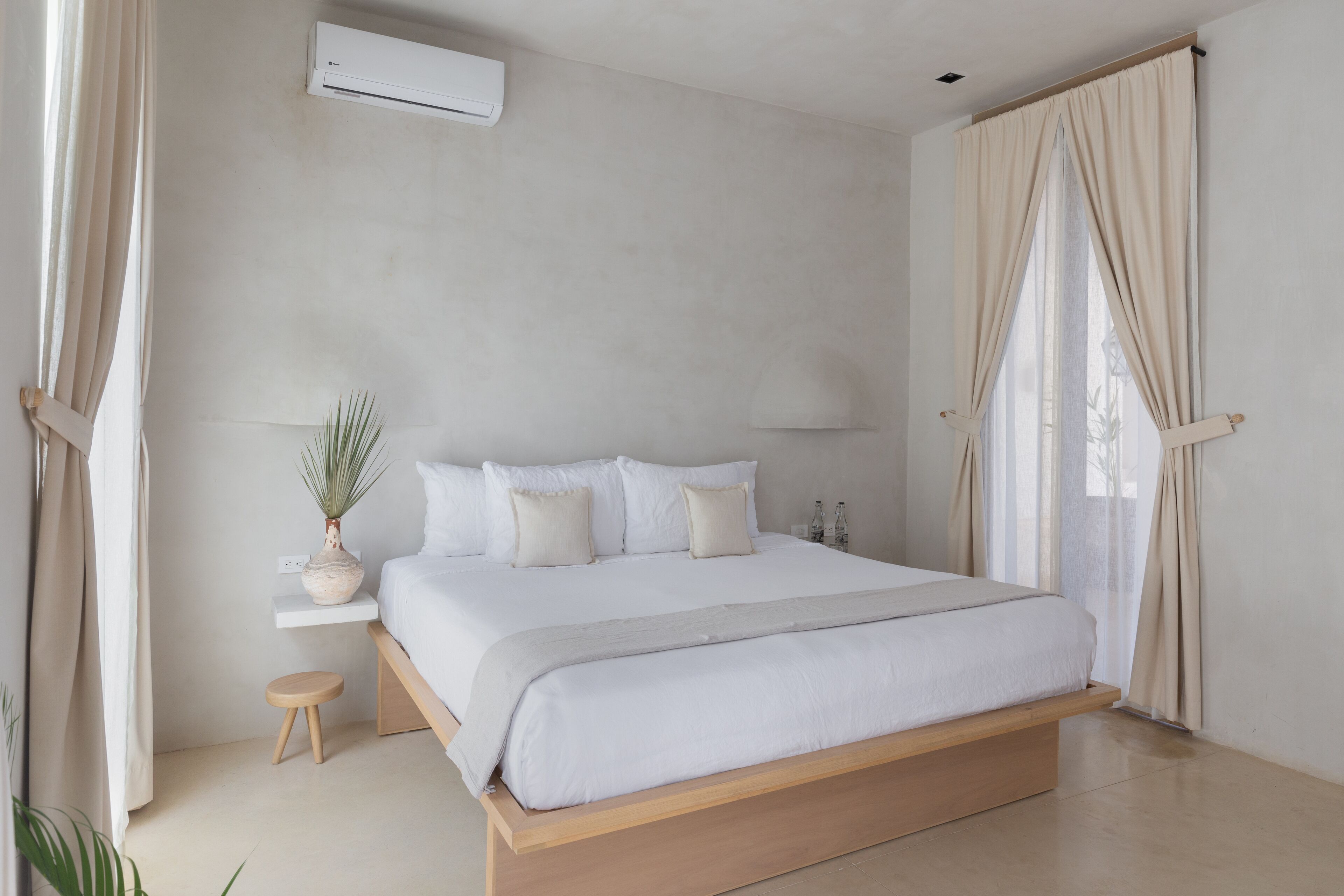 A minimalist bedroom with a large bed, bedside tables, a potted plant, and a window with curtains.