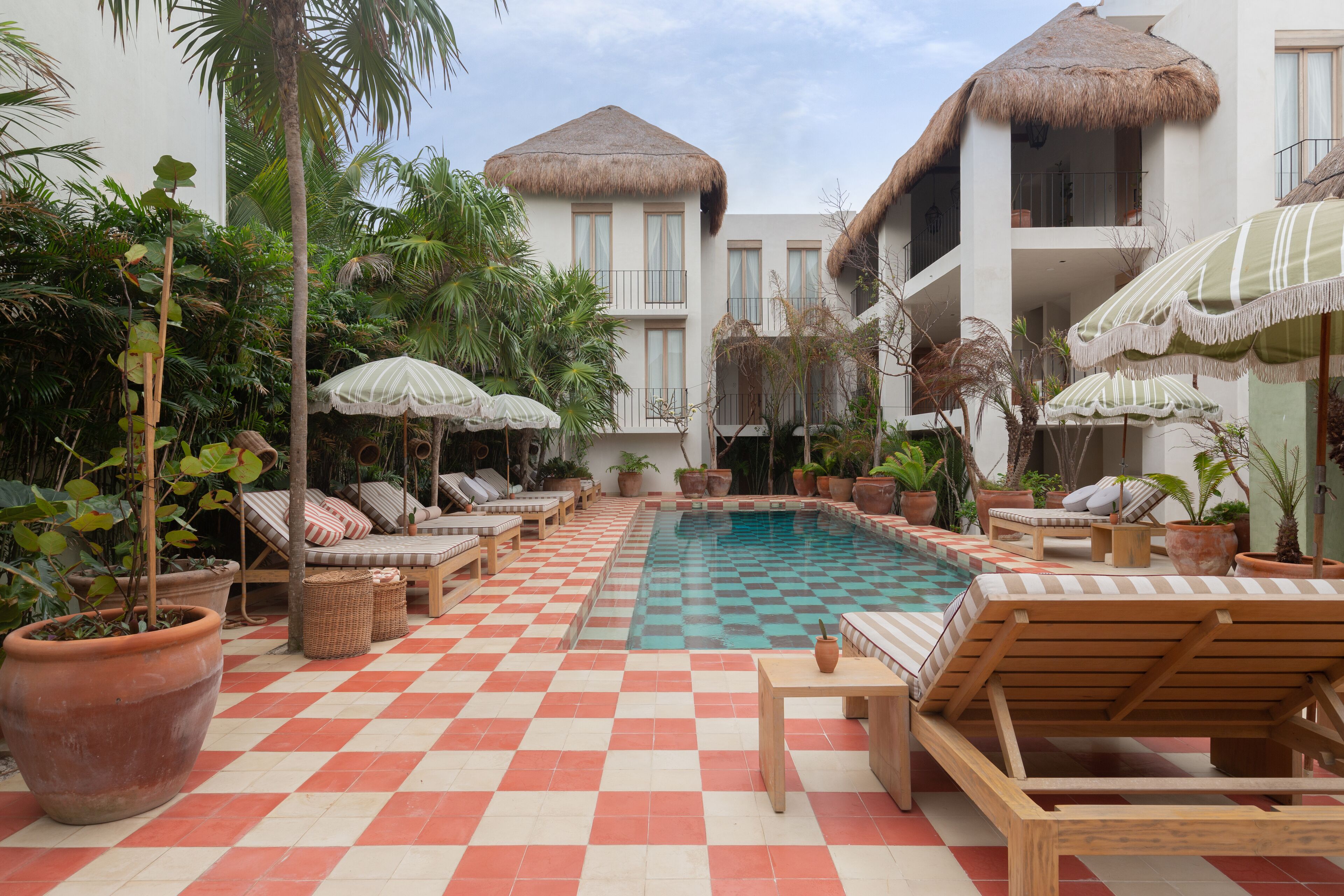 A pool area with checkered flooring, lounge chairs, and potted plants.
