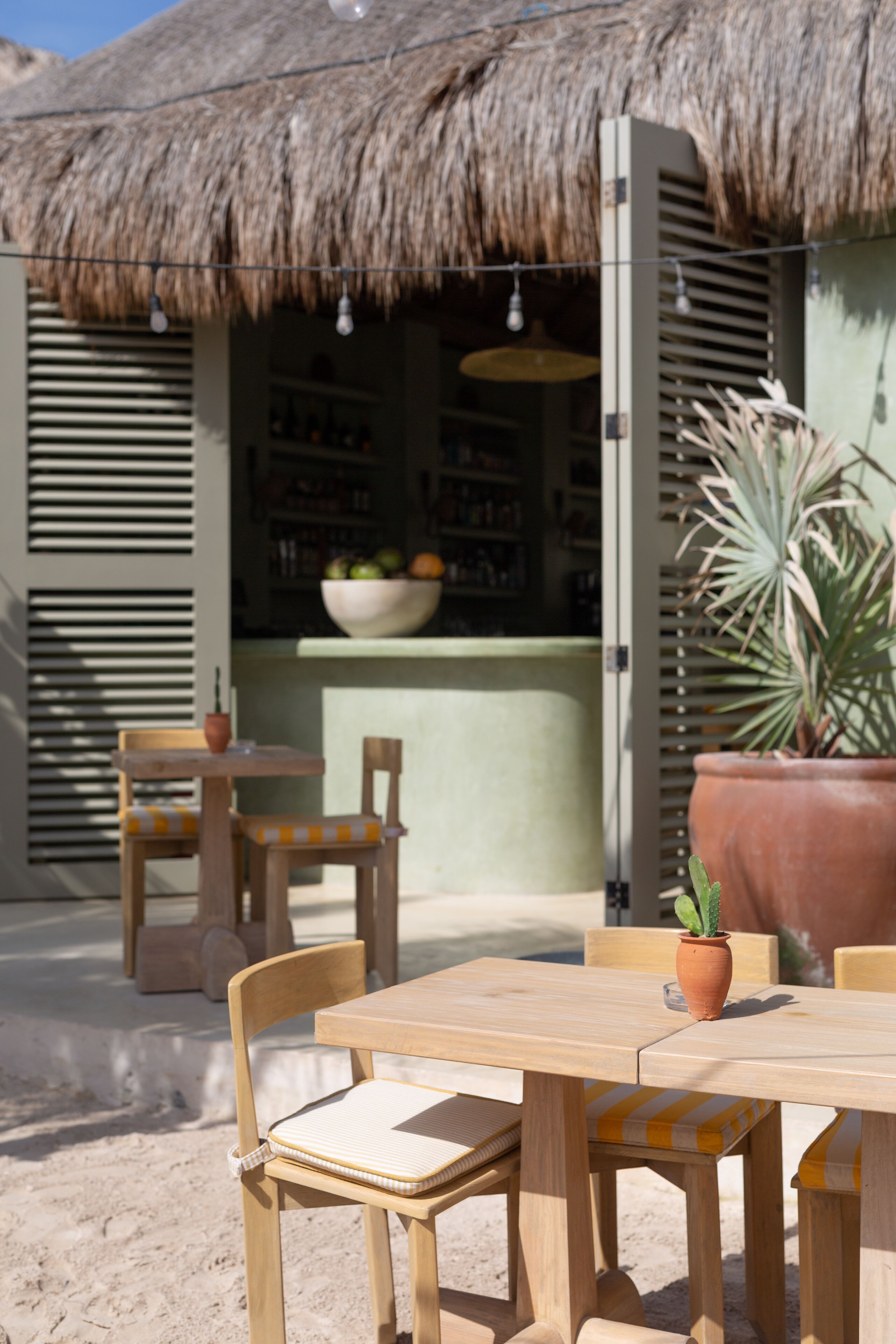 A wooden table and chairs set outside a building with a thatched roof.