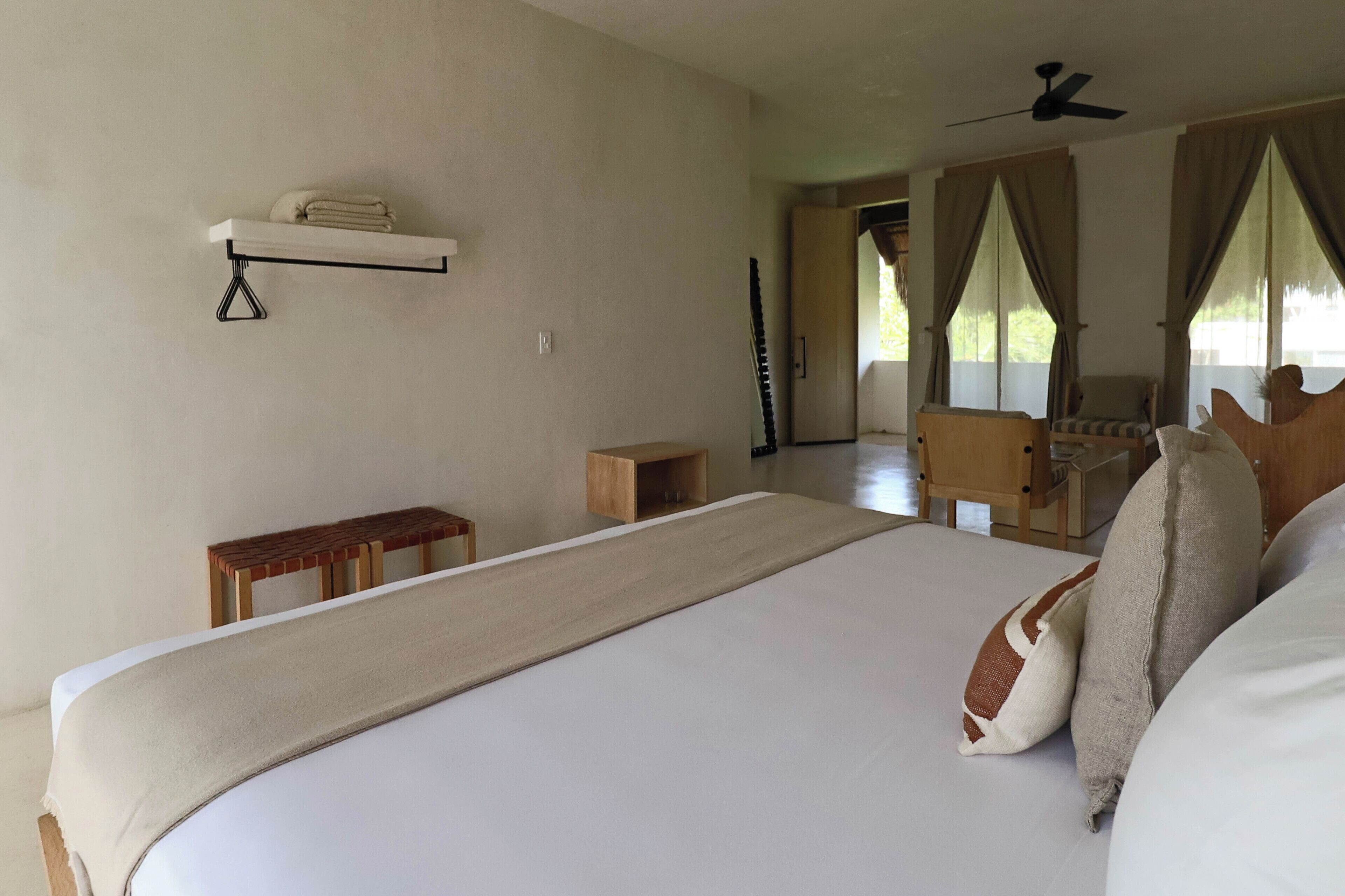 Ein Schlafzimmer mit einem großen Bett, einem Nachttisch, einem Regal mit Handtüchern, einem Holzsessel und einem Deckenventilator.