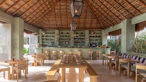 A spacious dining area with a long wooden table and benches, surrounded by shelves stocked with bottles and a bar area. - Hotel Panamera (Tulum)