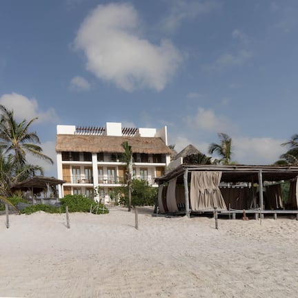 A beachfront hotel with multiple balconies, a thatched-roof structure, and palm trees.