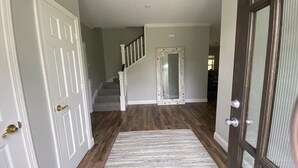 Un passadís amb sòl de fusta, una porta blanca i una escala que condueix a una altra habitació.