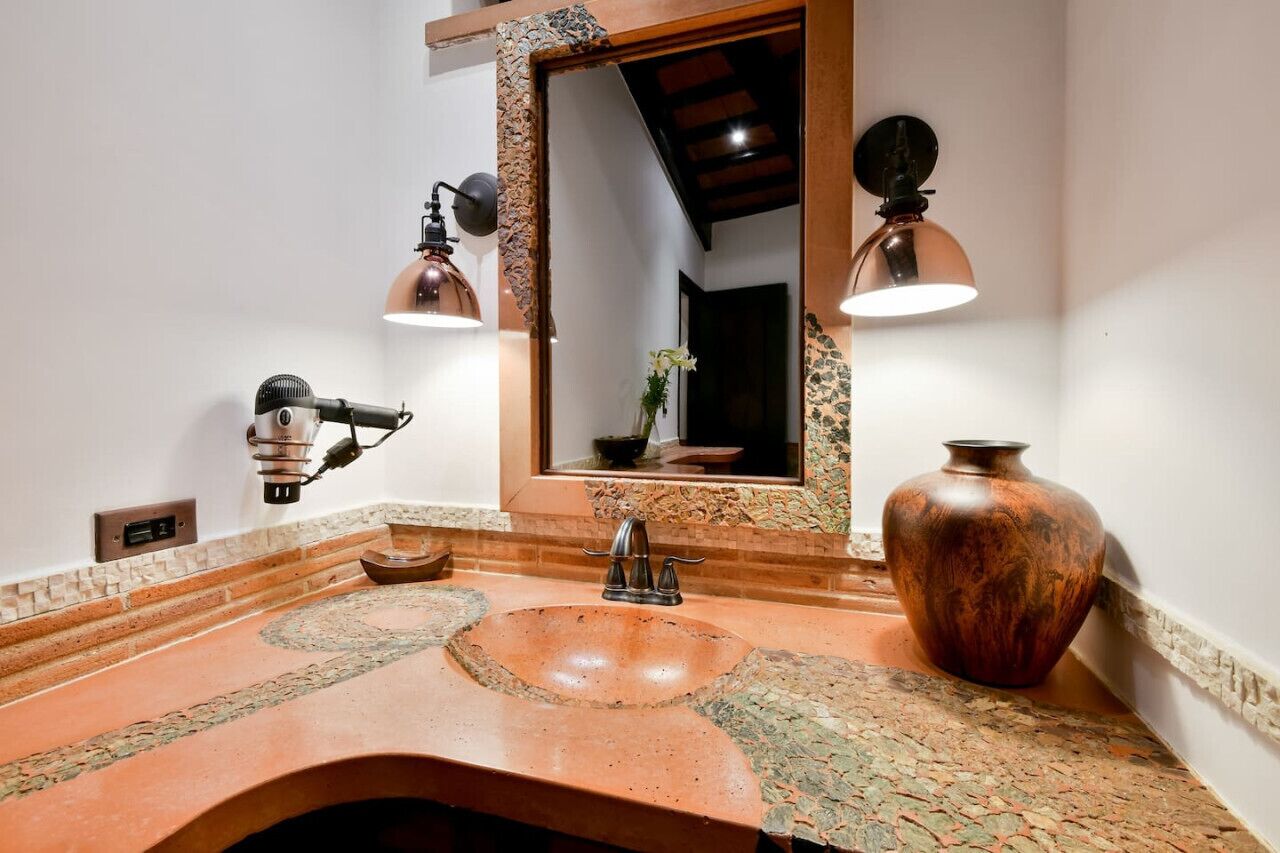 A bathroom with a large mirror, a sink with a unique design, and two wall-mounted lights.