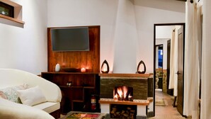 A cozy living room with a fireplace, a flat-screen TV mounted on a wooden wall, a sofa, and a coffee table.