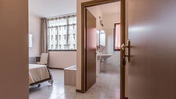 Een hotelkamer met een bed, een klein tafeltje, een raam met gordijnen, een badkamer met een wastafel en spiegel, en een deur.