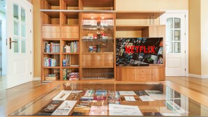 A room with wooden shelving units, a glass display table with brochures, and a wall-mounted Netflix screen. - VIRGEN DEL VALLE APARTMENT. -WINE ROUTE- 4 PEOPLE- 75M² (Cenicero)