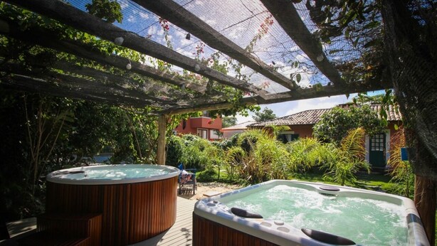 Una terraza de madera con dos jacuzzis, rodeada de exuberante vegetación y un pérgola.