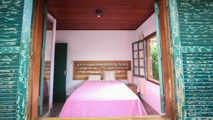 Una habitación con cama, techo de madera y ventana con vista a follaje.