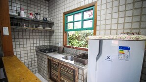 Cocina compacta con estufa a gas empotrada, un lavamanos y un refrigerador. Se observa una ventana con marco verde y una repisa sobre el lavamanos.