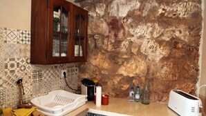 Une cuisine avec un mur en pierre, un meuble en bois, un évier blanc et un grille-pain.