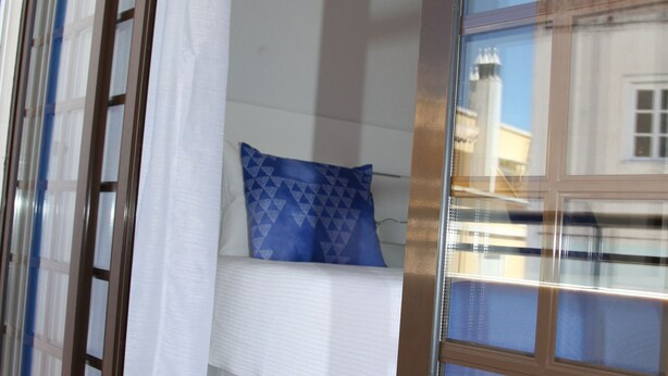 Une chambre à coucher avec un lit, un oreiller bleu et une fenêtre donnant sur des immeubles.