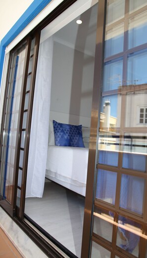 A bedroom with a bed, a blue pillow, and a window with a view of buildings.