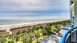 Een resort met uitzicht op het strand, een zwembad en een balkon met ligbedden.
