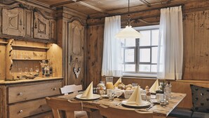 Un coin repas en bois avec une table dressée pour deux personnes, agrémenté d’un lustre ancien, d’une nappe blanche et d’un banc avec des coussins en forme de cœur.