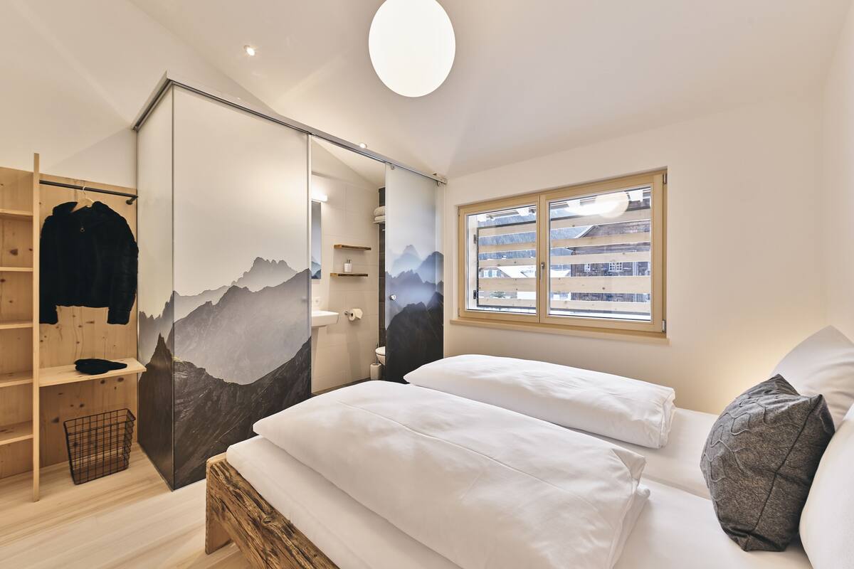 Un dormitorio con cama, armario, ventana y vistas a las montañas.