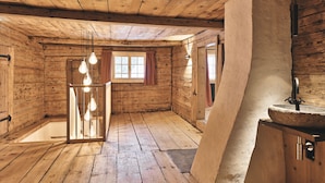 L’intérieur d’un chalet en bois, au style rustique, comprend un plancher en bois, une grande fenêtre avec des rideaux et un évier en pierre.