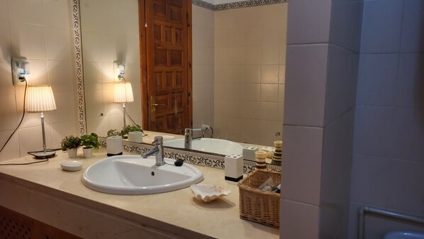 A bathroom with a double sink, a mirror, a wooden door, and a wall-mounted lamp.