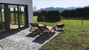 A modern house with a patio area featuring two wooden lounge chairs and a fire pit.