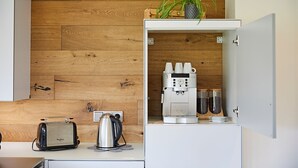 A compact kitchenette with a wooden wall, a coffee machine, a toaster, and a potted plant.