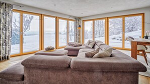 A cozy living room with a sectional sofa, a wooden dining table, and large windows offering a snowy view.