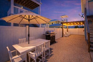 Patio esterno con tavolo e sedie, un barbecue, luci a catena e un'area salotto coperta.