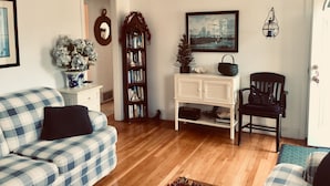 Ein Wohnzimmer mit einem karierten Sofa, einem weißen Konsolentisch, einem Bücherregal und einem gerahmten Gemälde an der Wand.