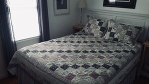 Ein ordentlich bezogenes Bett mit einem gemusterten Quilt, ein Nachttisch mit Lampe und ein gerahmtes Bild an der Wand.
