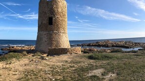 Uma torre de pedra com uma pequena janela, rodeada por terreno rochoso e céu claro.