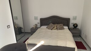 Quarto moderno com uma cama grande, uma mesinha de cabeceira, um criado-mudo, uma cadeira e um espelho.