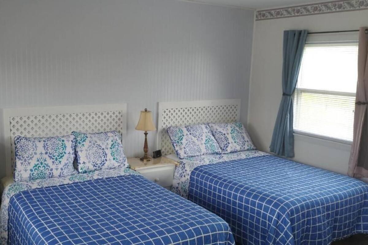 A bedroom with two beds, a nightstand, a dresser, a mirror, and a window with curtains.