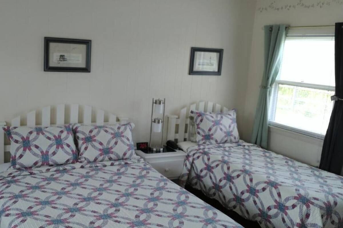 A bedroom with two beds, each with a patterned bedspread, a bedside table with a lamp, and a framed picture on the wall.