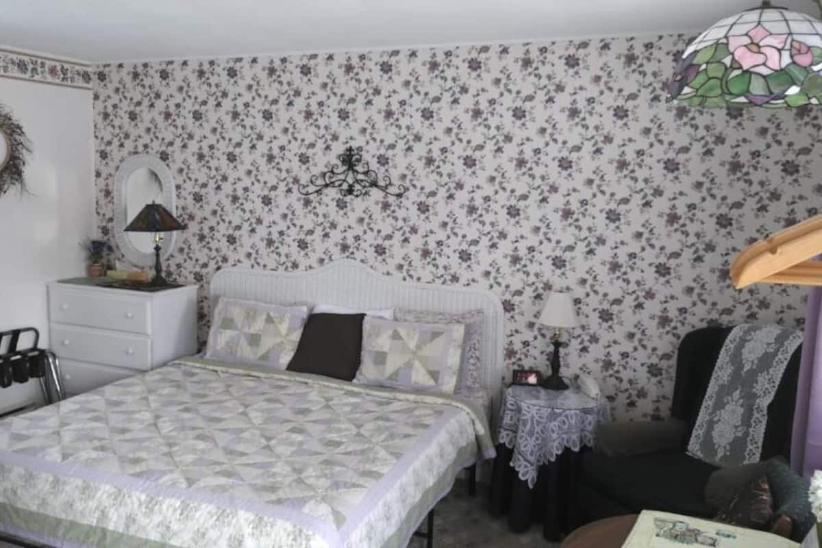 A bedroom with a bed, dresser, nightstand, and a floral-patterned wallpaper.