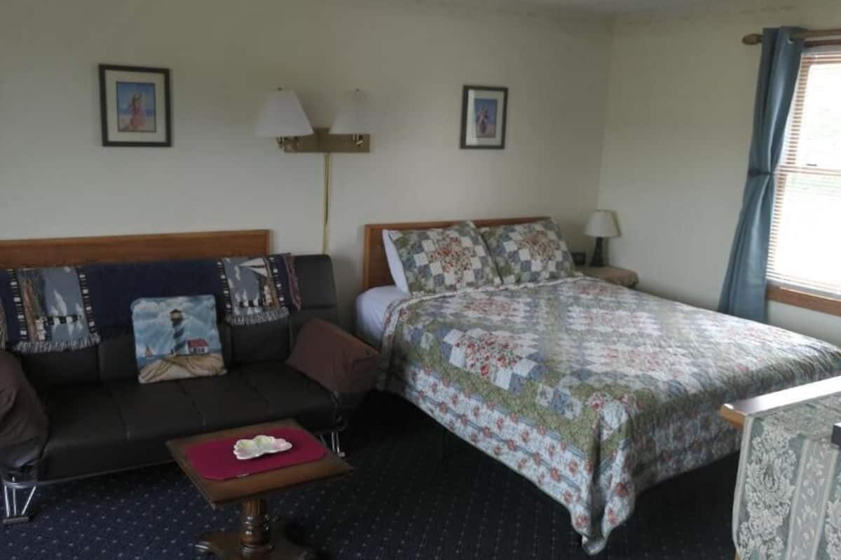 A hotel room with a bed, a sofa, a small table, and a lamp.