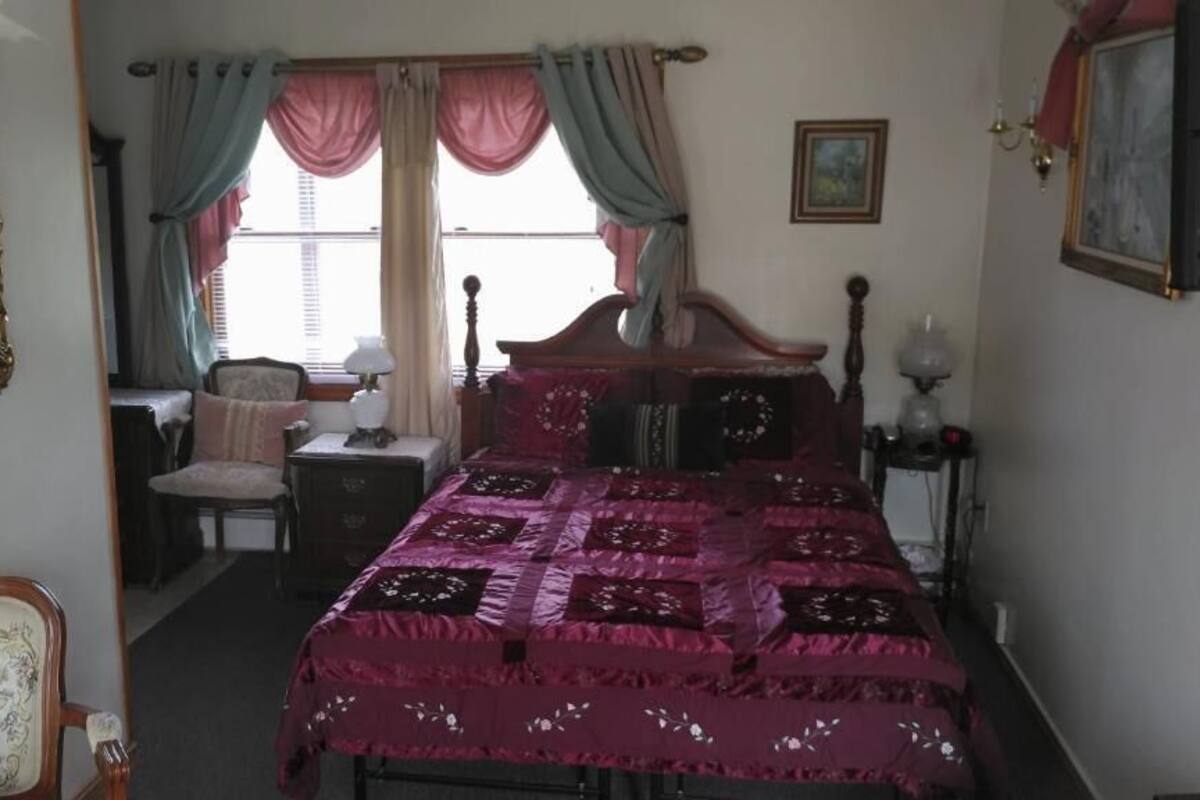 A bedroom with a large bed, a chair, a nightstand, and a dresser.